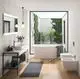 Badezimmer mit freistehender Badewanne und moderner Armatur von Ideal Standard. Fenster mit Pflanzen bietet natürlichen Lichteinfall. Holzfussboden und minimalistischer Stil.